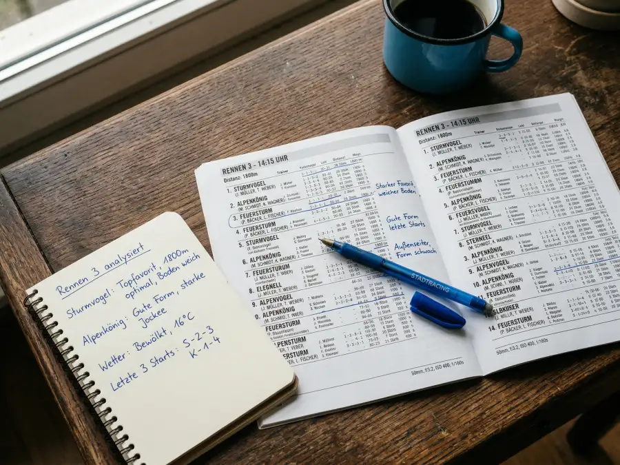 Aufgeschlagenes Rennprogramm mit handschriftlichen Notizen zur Formanalyse der Pferde auf einem hölzernen Tisch